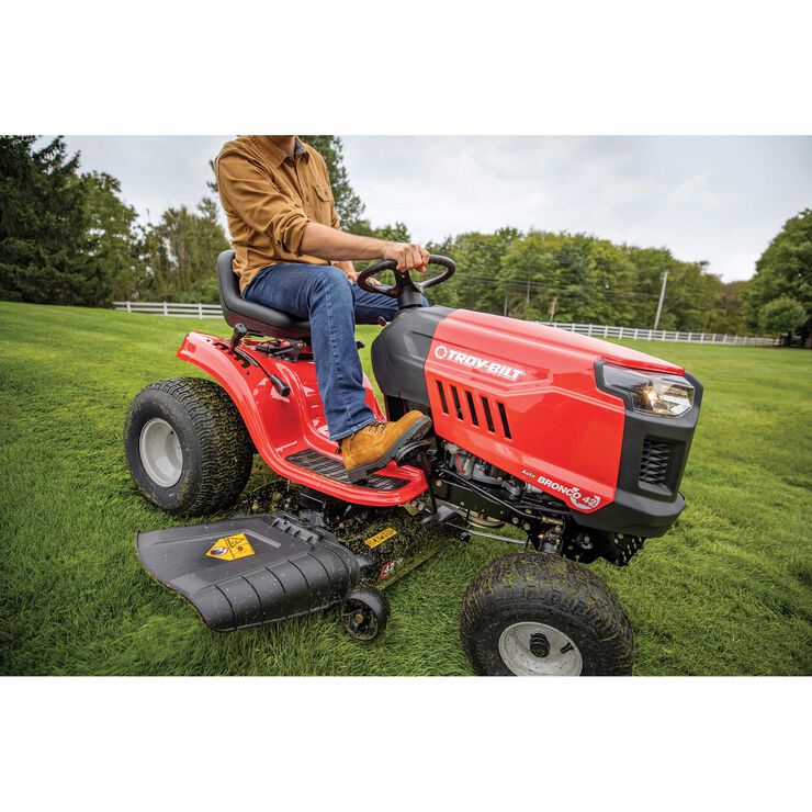 Person operating a red riding lawn mower on a grassy field with trees in the background